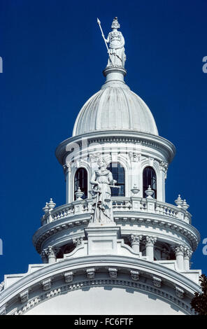 A statue of Minerva, the Roman Goddess of Wisdom, stands atop the cupola of the ornate Merced County Courthouse Museum in Merced, California, USA. The historic three-story courthouse was built in 1875 in Italianate style and became a county museum after a new modern Merced courthouse was built in 2007. The lower statue is one of three on the older building that depicts Justitia, the Roman Goddess of Justice. Stock Photo