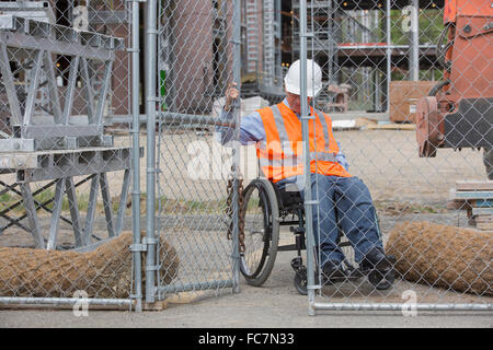 Caucasian engineer in wheelchair opening construction site gate Stock Photo