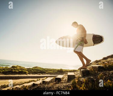 Caucasian man carrying surfboard on beach Stock Photo