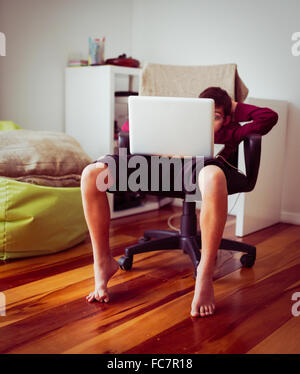 Mixed race boy using laptop in chair Stock Photo