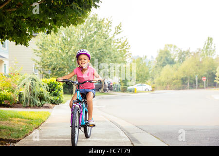 Mixed race girl riding bicycle on sidewalk Stock Photo