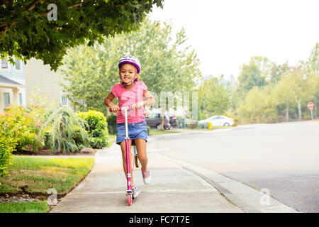 Mixed race girl riding scooter on sidewalk Stock Photo