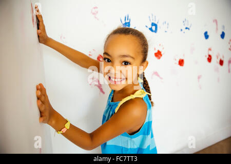 Mixed race girl making hand prints on wall Stock Photo