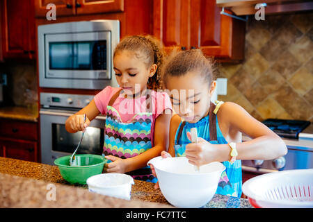 Mixed race sisters cooking in kitchen Stock Photo