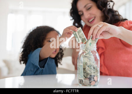 Mother and daughter saving money in jar Stock Photo