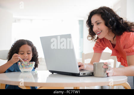 Mother using laptop at breakfast with daughter Stock Photo