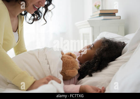 Mother tucking daughter into bed Stock Photo