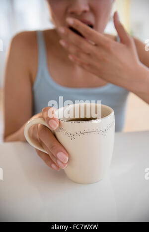 Yawning Hispanic woman drinking coffee Stock Photo
