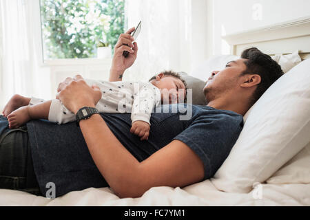 Father using cell phone with sleeping baby son Stock Photo