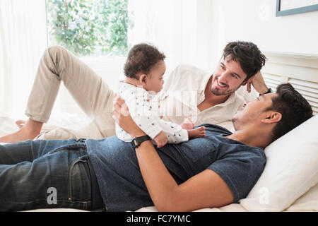 Gay fathers playing with baby son on bed Stock Photo