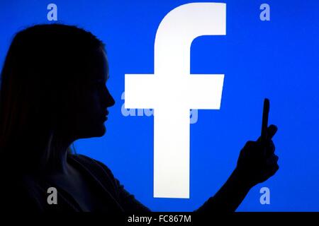 A woman's silhouette with a smartphone in front of a facebook logo, 12 January 2016. Stock Photo