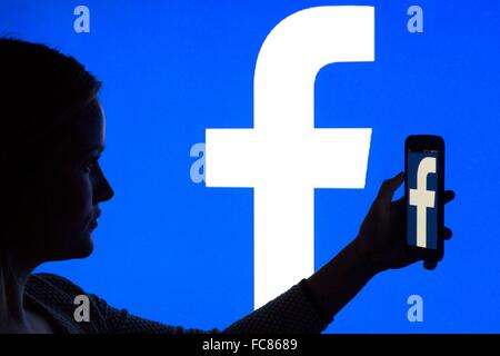 A woman's silhouette with a smartphone in front of a facebook logo, 12 January 2016. Stock Photo