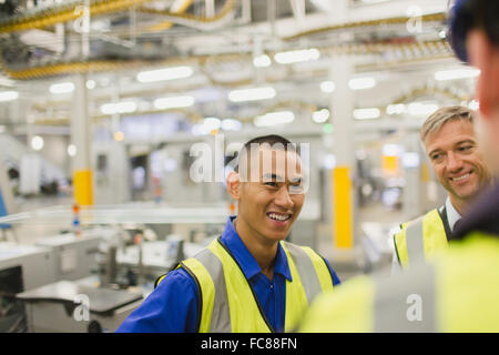 Workers in reflective clothing talking in factory Stock Photo