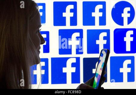 A woman's silhouette with a smartphone in front of  facebook logo's, 12 January 2016. Stock Photo