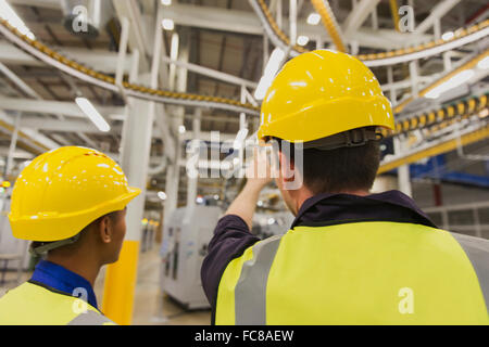 Workers discussing printing press conveyor belts overhead Stock Photo