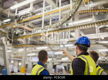 Workers discussing winding printing press conveyor belts overhead Stock Photo