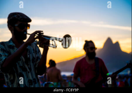 RIO DE JANEIRO - FEBRUARY 21, 2015: Silhouette of a musician playing his horn to an audience at the popular Arpoador sunset spot Stock Photo