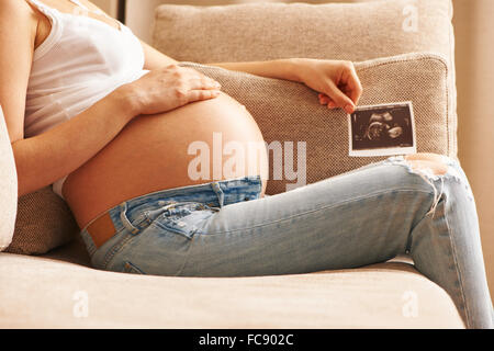 Pregnant woman at home holding ultrasound scan Stock Photo