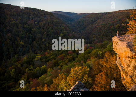 In the hills of Arkansas, a man stands on the edge of a rock overlook enjoying the views of colorful trees below. Stock Photo