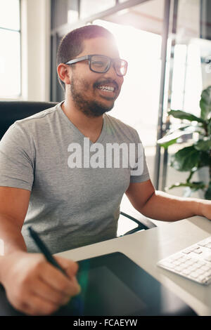 Happy graphic designer working in his own office. He is using digitized graphic tablet and digital pen for editing. Stock Photo