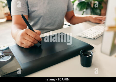 Graphic designer using digital tablet and desktop computer in the office. Close-up of designer's hand working with pen. Stock Photo