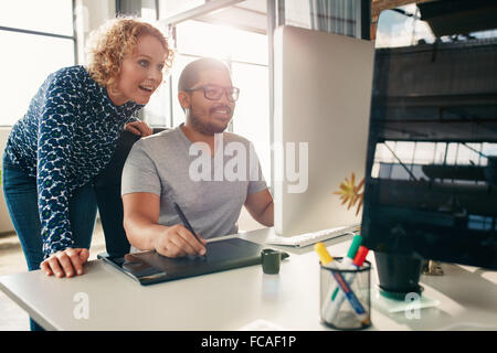 Two young creative people working together on a new project in office. Male and female designer using digital graphic tablet and Stock Photo