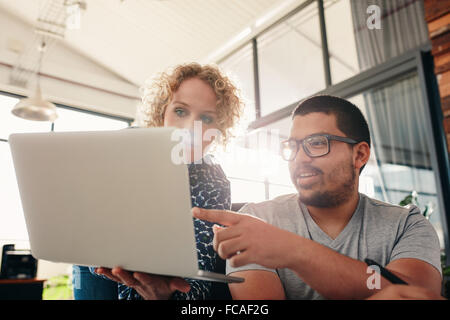 Two young graphic designers working in their own office. Man pointing at laptop in women's hands. Stock Photo