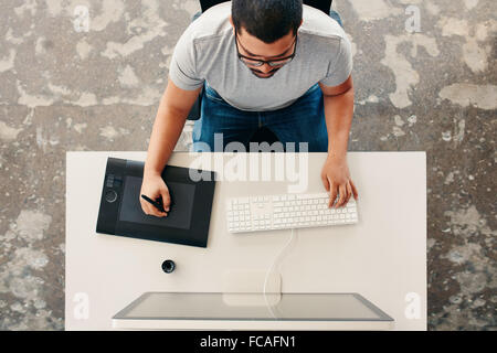 Top view of a male graphic designer using digital graphics tablet and desktop in the office. Editor sitting at his desk drawing Stock Photo