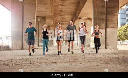 Portrait of group of runners from running club under a bridge. Young men and women jogging together. Stock Photo