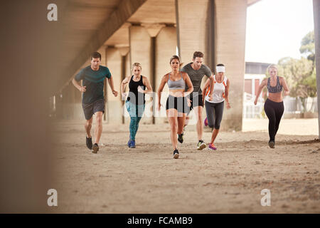 Portrait of group of runners in fitness clothing running under a bridge. Young men and women doing running work out together. Stock Photo
