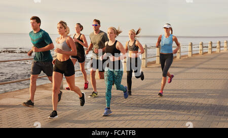 Portrait of young people running along the beach boardwalk by the ocean. Fit young men and women running training outdoors by th Stock Photo