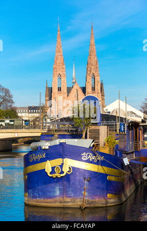 Floating bar on barge at Quai des Pecheurs  on Ill river and St Paoul Church in the background Strasbourg Alsace France Stock Photo