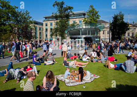 Sunbathers and pedestrians enjoying the Summer sunshine in St Andrew Square Edinburgh with Harvey Nichols in the background. Stock Photo