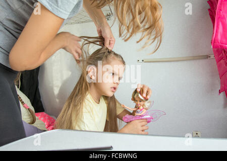 Six year old girl playing in the doll while mom pigtail braids of hair, in the second-class train carriage Stock Photo