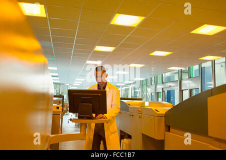 Worker in lab coat at computer among printers in printing plant Stock Photo