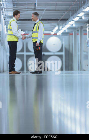 Businessmen in reflective clothing shaking hands in printing plant Stock Photo