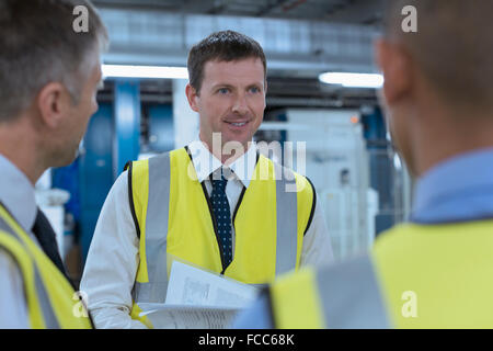 Workers in reflective clothing talking in factory Stock Photo