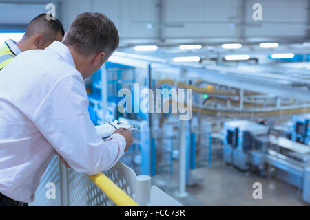 Workers leaning on railing overlooking factory Stock Photo