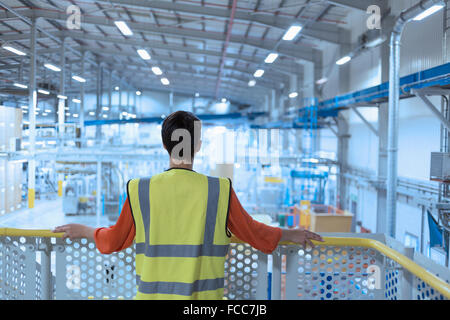 Worker in reflective clothing on platform looking out over factory Stock Photo