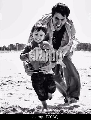 Father Playing Rugby Game With Son On Beach
