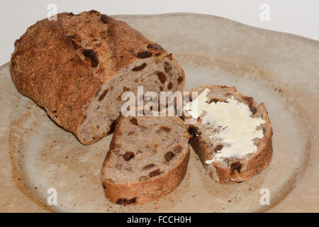 Loaf and slices, one buttered,  slices of whole wheat pecan raisin bread on plate Stock Photo