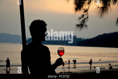 Silhouette of man holding glass of rose wine at sunset on the beach Stock Photo