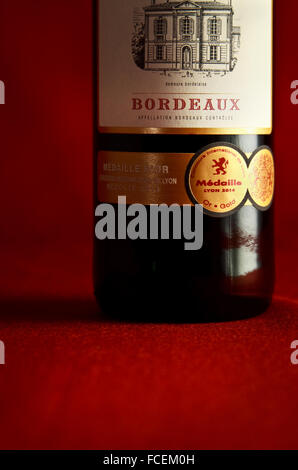 A single bottle of French Bordeaux wine on a crimson base and backdrop.