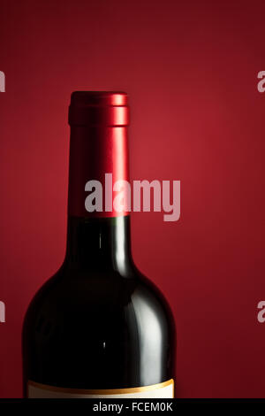 A single bottle of French Bordeaux wine on a crimson base and backdrop.