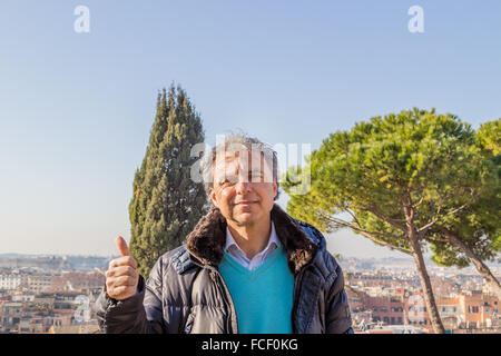 Middle-aged Caucasian man with gray hair dressed in black down jacket making thumbs up Stock Photo