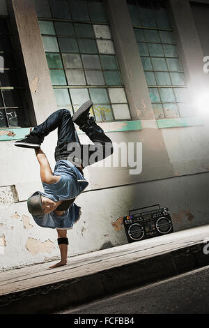 A young man breakdancing on the street of a city, doing a one handed handstand. Stock Photo