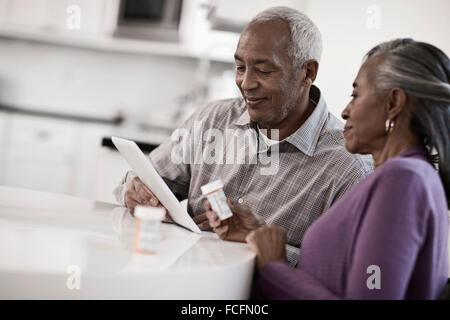 A grey haired couple sitting at a table, looking at information on a digital tablet. Stock Photo