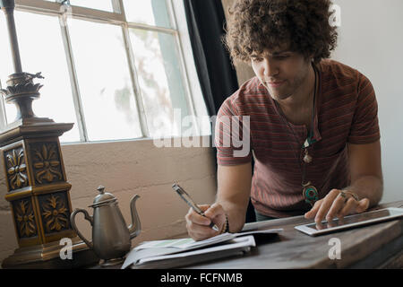Loft living. A man seated by  window, using a pen and paper and a digital tablet. Stock Photo
