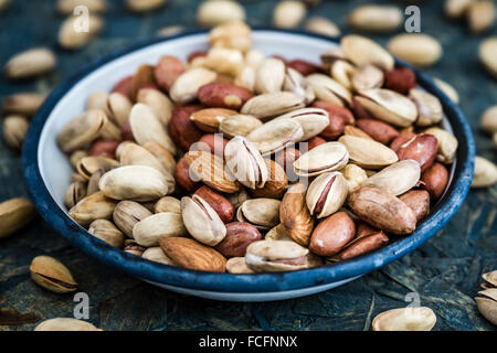 Pistachios, nuts, almonds, hazelnuts in white enamel plate on blue wooden background Stock Photo