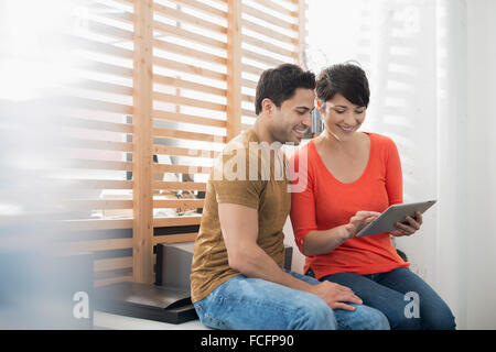 A couple sitting by a window using a digital tablet. Stock Photo